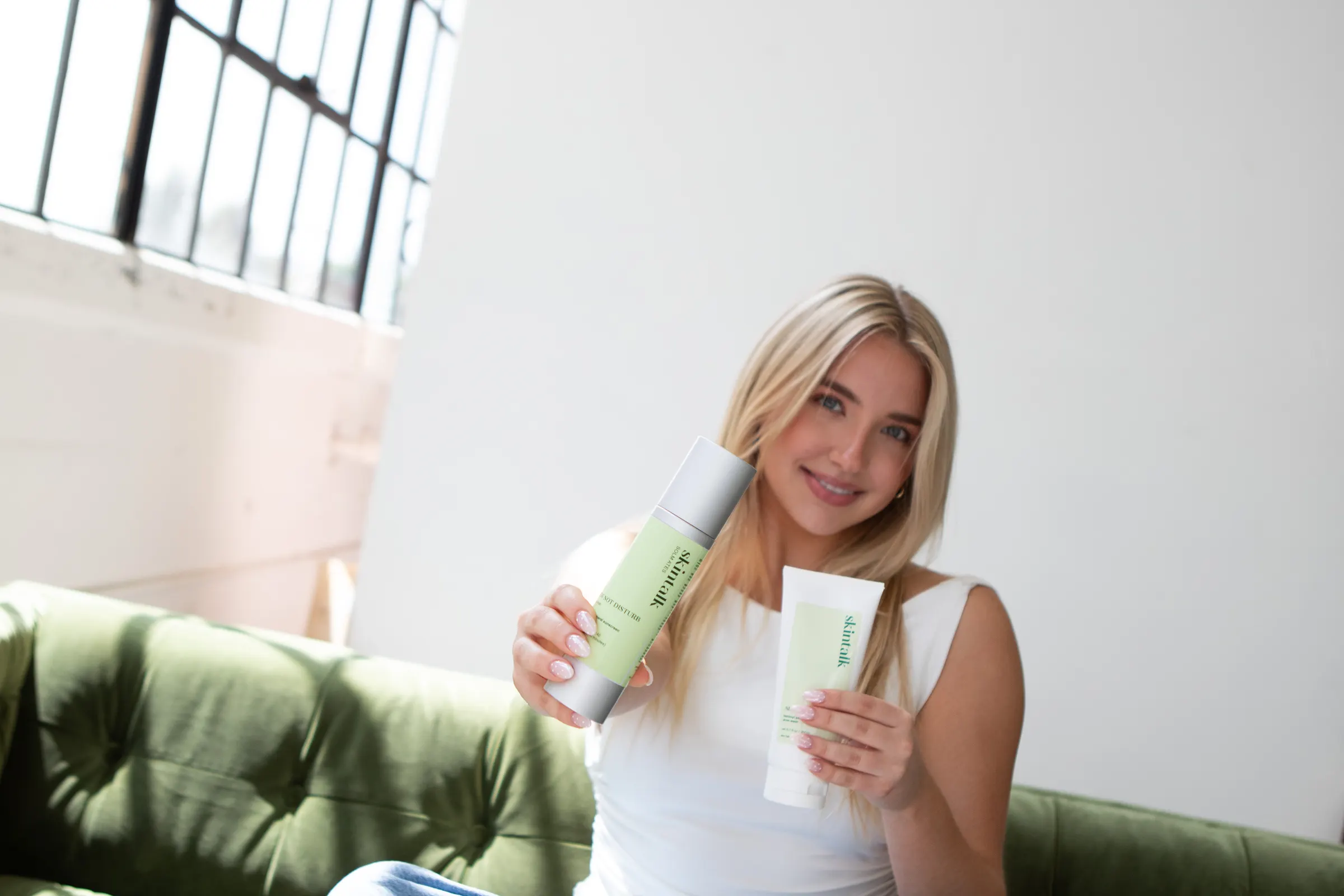 Skin Talk guest on a green sofa holding two Skin Talk skincare products